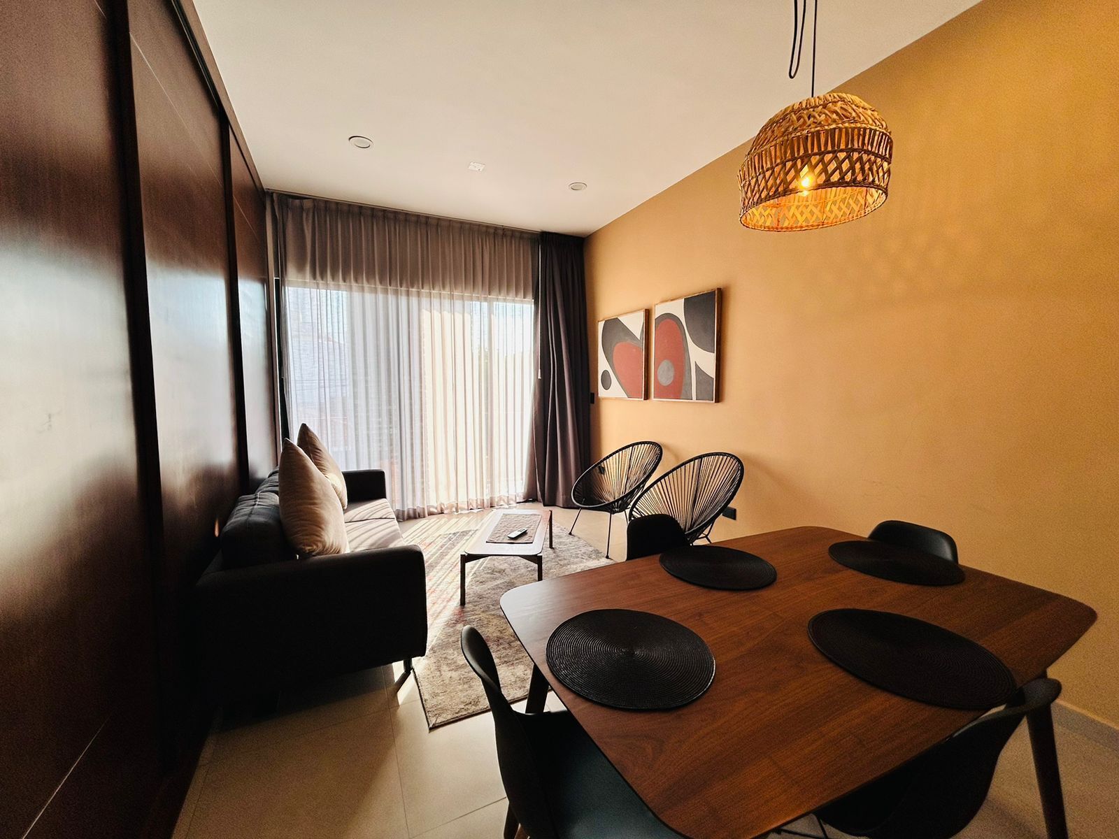 A modern dining area with a wooden table, black chairs, and a woven pendant light.