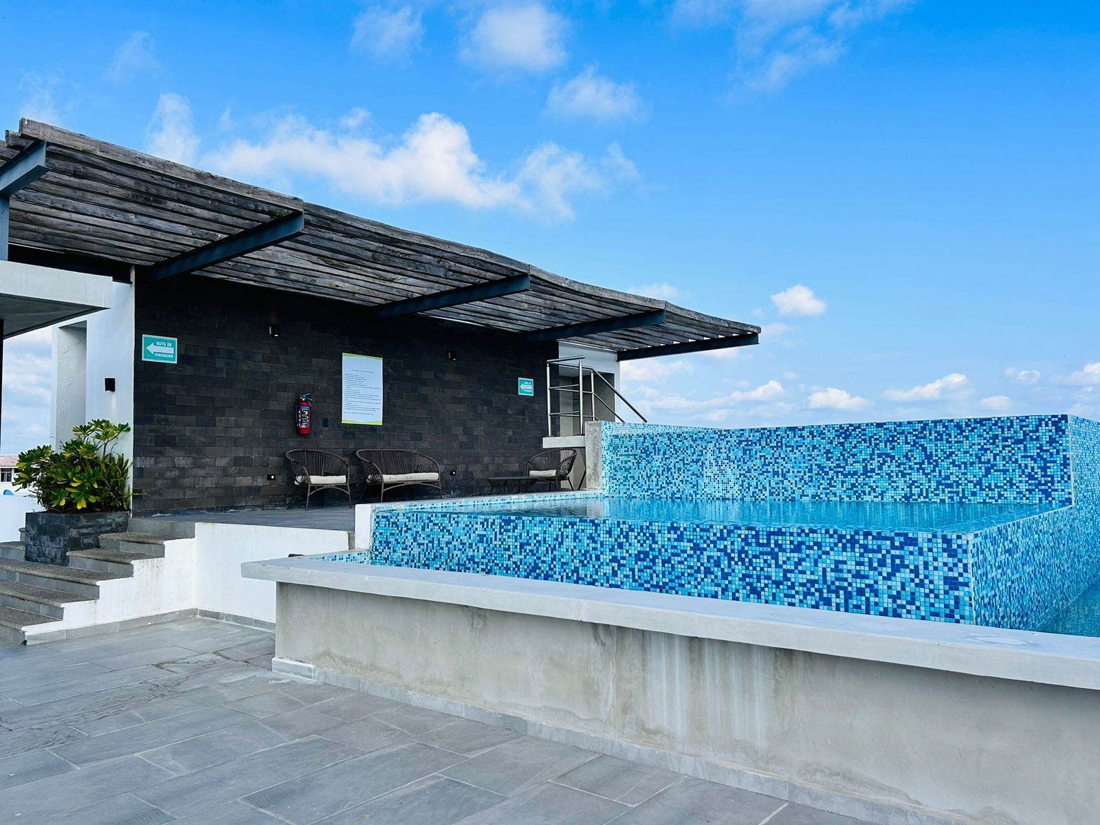 Piscina exterior moderna, com borda em azulejo, área de estar coberta e escadaria para um nível superior.