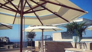 A rooftop terrace with lounge chairs, a bar area, and umbrellas. - Sea Glass Escape (Rafailovići)