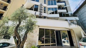 A multi-story hotel with a modern design, featuring balconies on each floor and a central entrance with glass doors. - Sea Glass Escape (Rafailovići)