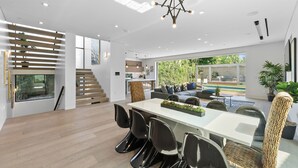 Et moderne interiør med spiseområde, trappe og store vinduer med udsigt over naturen.