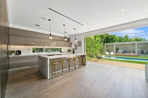 Eine moderne Küche mit Marmorarbeitsplatte, Barhocker, Pendelleuchten und Blick auf einen Swimmingpool.