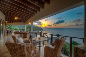Una terrazza con mobili in vimini, un tavolino con bevande e vista sul mare al tramonto.