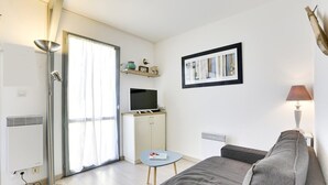 A modern living room with a sofa, a television on a cabinet, a floor lamp, and a picture frame on the wall. - Seignosse-océan Villa Patio 4 Personnes (SEIGNOSSE)