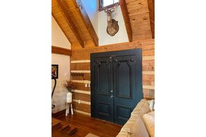 A wooden interior with a dark blue double door, wooden beams on the ceiling, and a beige sofa.