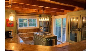 A kitchen with wooden beams, a central island, a stove, and a large window.