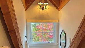 A small, rustic bathroom with a wooden ceiling, a window with a view of trees, a sink, and a mirror.