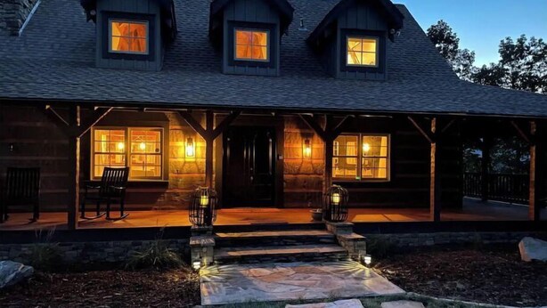 A log cabin with a stone porch, multiple windows, and a stone pathway leading to the entrance.