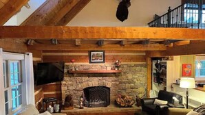 A cozy living room with a stone fireplace, wooden beams, a mounted deer head, and a comfortable seating area.