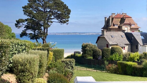 Una casa sul lungomare con un grande albero in primo piano, un prato curato e vista mare.