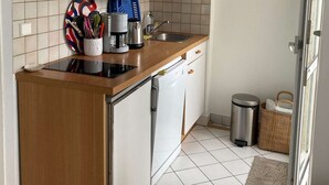 Una cucina compatta con mobili bianchi, un forno a microonde, un lavello e un piccolo cestino.