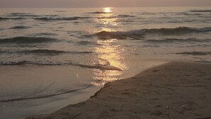 Ein Strandbild mit untergehendem Sonnenuntergang über dem Meer, sanfte Wellen umspülen das Ufer.