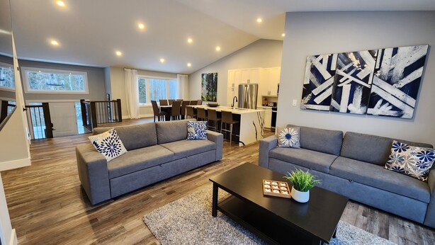 Ein modernes Wohnzimmer mit zwei grauen Sofas, einem Couchtisch und einem Essbereich, im Hintergrund ist eine Küche zu sehen.