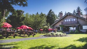 Ein Restaurant mit Terrassensitzgelegenheiten, umgeben von Bäumen und einem gepflegten Rasen.