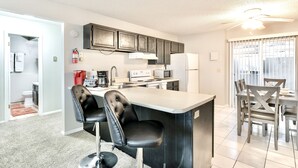 A modern kitchen with a bar area, a dining table with chairs, and a ceiling fan. - The Hygge apt C (Colorado Springs)
