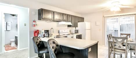 A modern kitchen with a bar area, a dining table with chairs, and a ceiling fan.