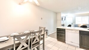 A dining area with a table set for six, a ceiling fan, and a kitchen with a dishwasher. - The Hygge apt C (Colorado Springs)