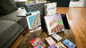 Uma sala de estar com uma mesa de centro que exibe diversos jogos de tabuleiro e um livro intitulado "The Hygge Game".