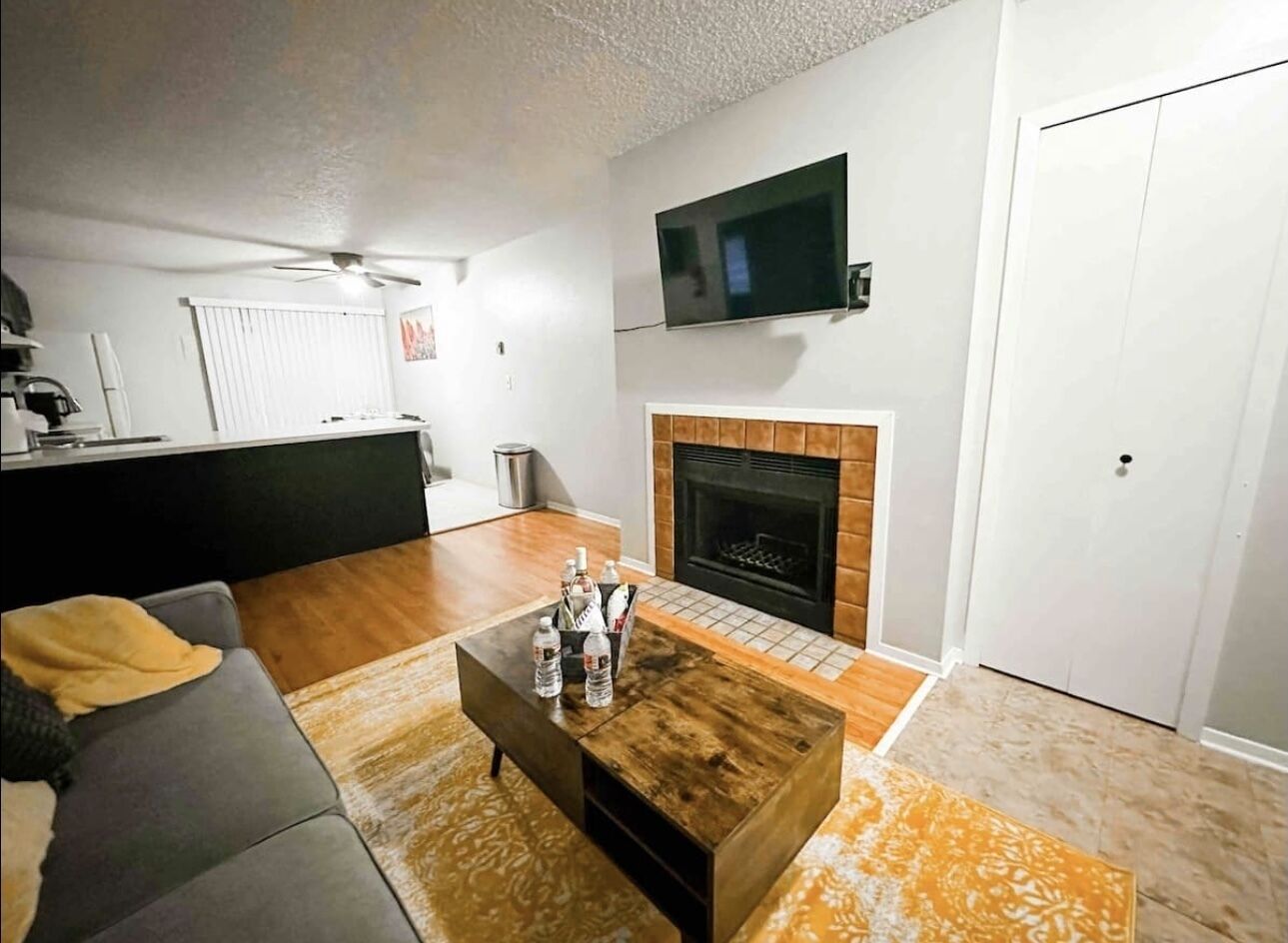 A living room with a fireplace, a television mounted above it, and a coffee table with bottles.