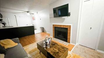 A living room with a fireplace, a television mounted above it, and a coffee table with bottles.