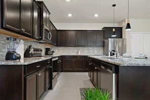 Una cocina moderna con armarios oscuros, encimera de granito y electrodomésticos de acero inoxidable.