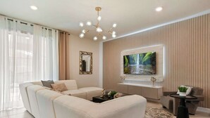 A modern living room with a sectional sofa, a flat-screen TV mounted on a wall, a decorative mirror, and a chandelier. - Grand Marvel & Star Wars Villa | Windsor Island (Davenport)