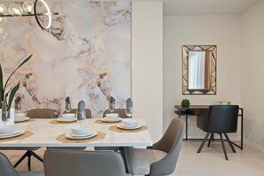 Un comedor moderno con una pared de mármol, una mesa de comedor dispuesta con platos, vasos y cubiertos, y un espejo en la pared.
