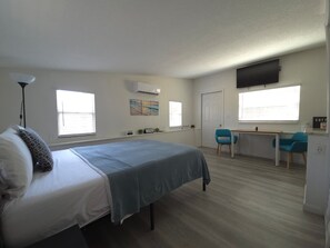 Ein Schlafzimmer mit einem Bett, einem Schreibtisch, zwei Stühlen, einem Fernseher und einem Fenster.