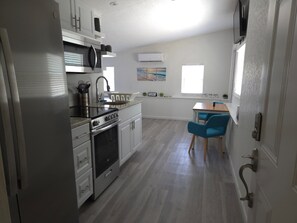 A compact kitchen with a stove, microwave, and sink, a dining area with a table and chairs, and a window with a view.