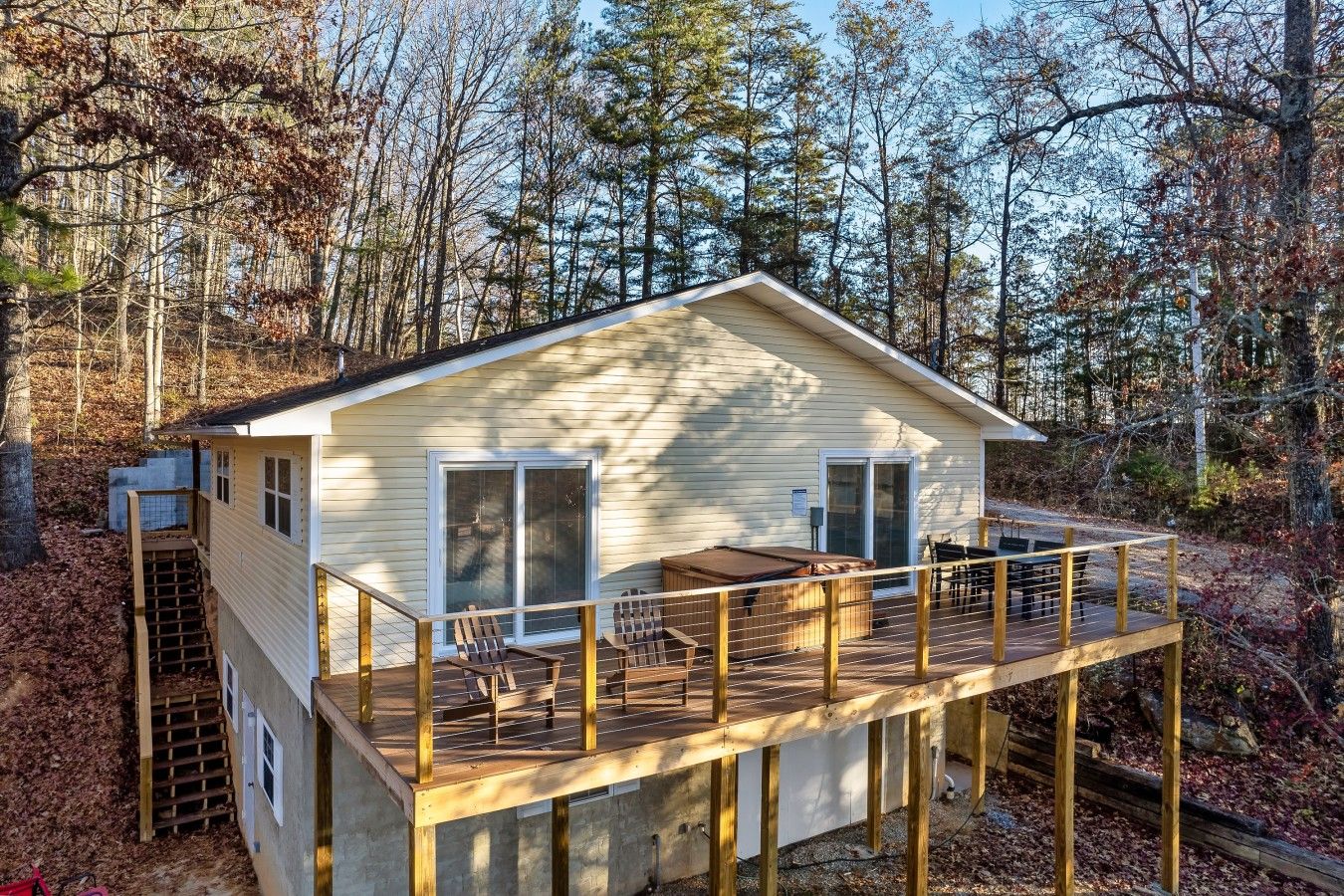 A cabin with a deck, a covered outdoor seating area, and a small staircase leading to an upper level.