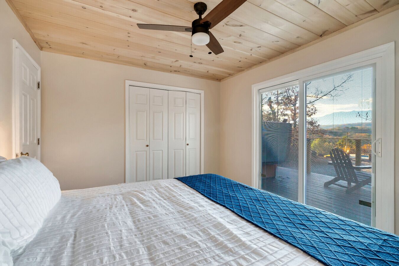 Une chambre à coucher avec un lit, un ventilateur de plafond, une porte blanche et une porte-fenêtre coulissante donnant sur un balcon.
