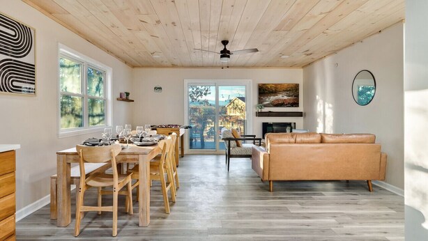 Un vaste espace de vie doté d’un plafond en bois, d’une table à manger avec des chaises, d’un canapé en cuir et d’une cheminée.