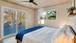 Une chambre à coucher avec un lit, un ventilateur de plafond et de grandes fenêtres donnant sur la forêt.