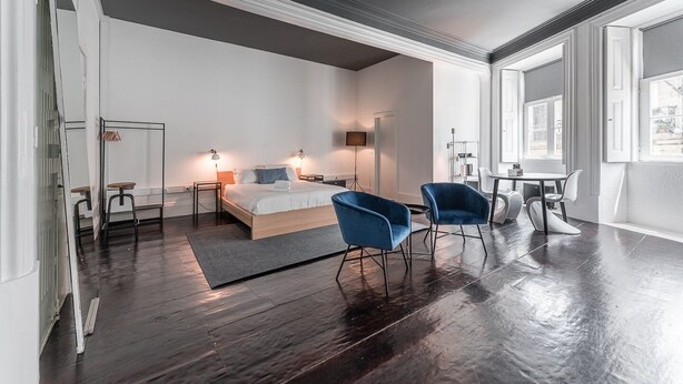 Ett modernt hotellrum med en stor säng, två blå fåtöljer, ett litet bord och ett skrivbord.