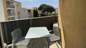 A balcony with a table and two chairs, overlooking a residential area with buildings and a tree. - Appartement T2 avec terrasse et parking couvert à proximité de la plage (LE CAP D AGDE)