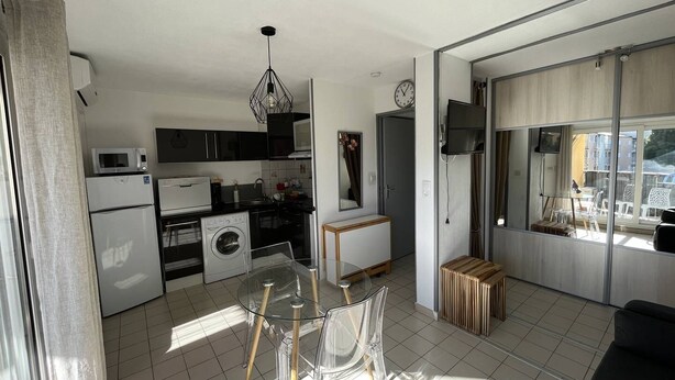A modern kitchen with a dining area, a washing machine, and a TV. - Appartement T2 avec terrasse et parking couvert à proximité de la plage (LE CAP D AGDE)