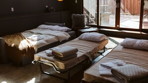 Ett rum med tre sängar placerade i en rad, ett fönster med utsikt över omgivningen och en hängande lampa.
