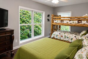 Une chambre avec un lit superposé, une commode, un téléviseur et une grande fenêtre donnant sur un paysage verdoyant.