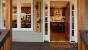 Une façade en bois avec une pancarte d’accueil, une cuisine visible à travers une porte vitrée et un paillasson.