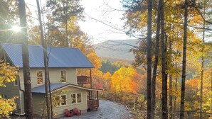 Une cabane dotée d’un porche et d’une petite terrasse, entourée d’une forêt aux couleurs automnales.