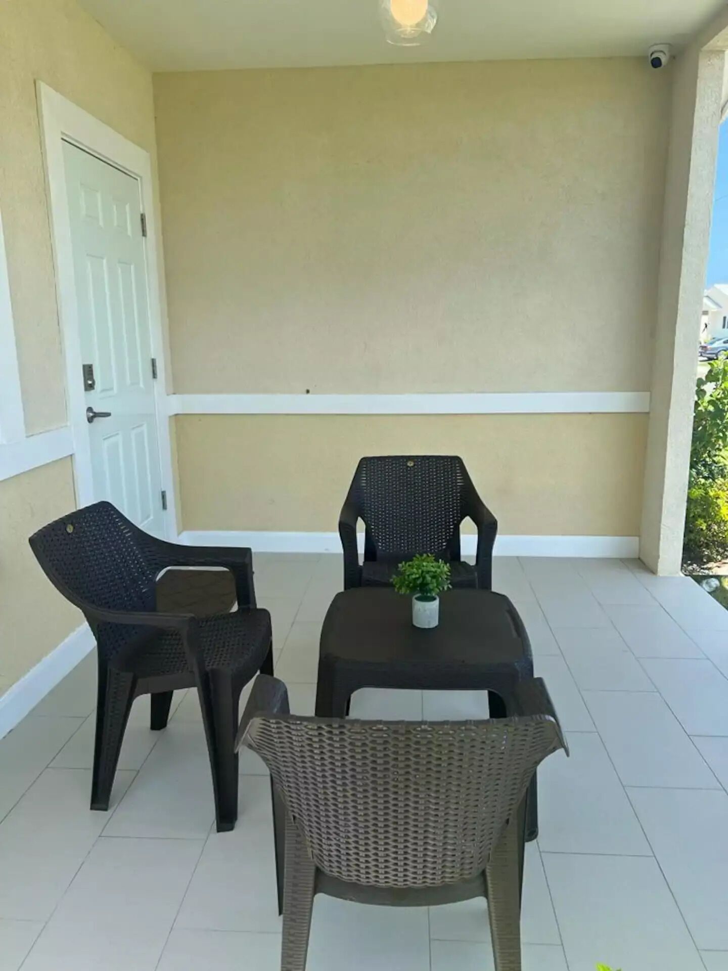 A small outdoor patio with a table and four chairs, a potted plant on the table, and a white door to the left.