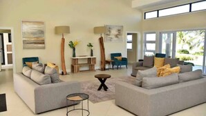 Un saló modern amb dos sofàs grisos, una taula de centre i un moble de televisió. Hi ha dues cadires, una taula petita i una finestra gran amb vista a zones verdes.