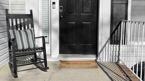 Un portico con una porta nera, una cassetta delle lettere, una panchina e un tappetino d'ingresso.
