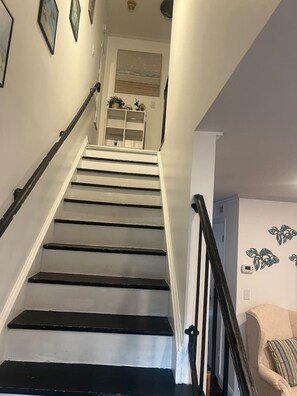 Uma escadaria com degraus pretos e paredes brancas, que leva a um quarto com uma porta branca e um termostato fixado na parede.