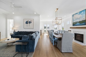 A modern living room with a dark blue sofa, a coffee table, and a dining area with a wooden table and chairs.