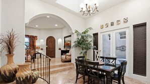 Ein geräumiges Foyer mit einer Marmortreppe, einem Essbereich mit Tisch und Stühlen sowie einer großen Topfpflanze.