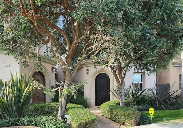 Un bâtiment avec un grand arbre devant, un chemin pavé et un panneau indiquant la présence d’un agent de sécurité assurant une surveillance vidéo en direct.