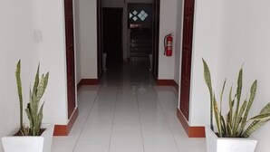 A hallway with white tiled floors, a fire extinguisher on the right wall, and two potted plants on either side. - Ban Saylomleng Residence (Vientiane)