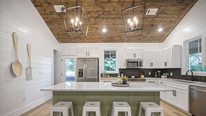 A modern kitchen with white cabinetry, a large island with stools, stainless steel appliances, and pendant lighting.