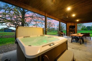 Een bubbelbad in een overdekte buitenruimte met een tafel, stoelen, een open haard en uitzicht op het omliggende landschap.